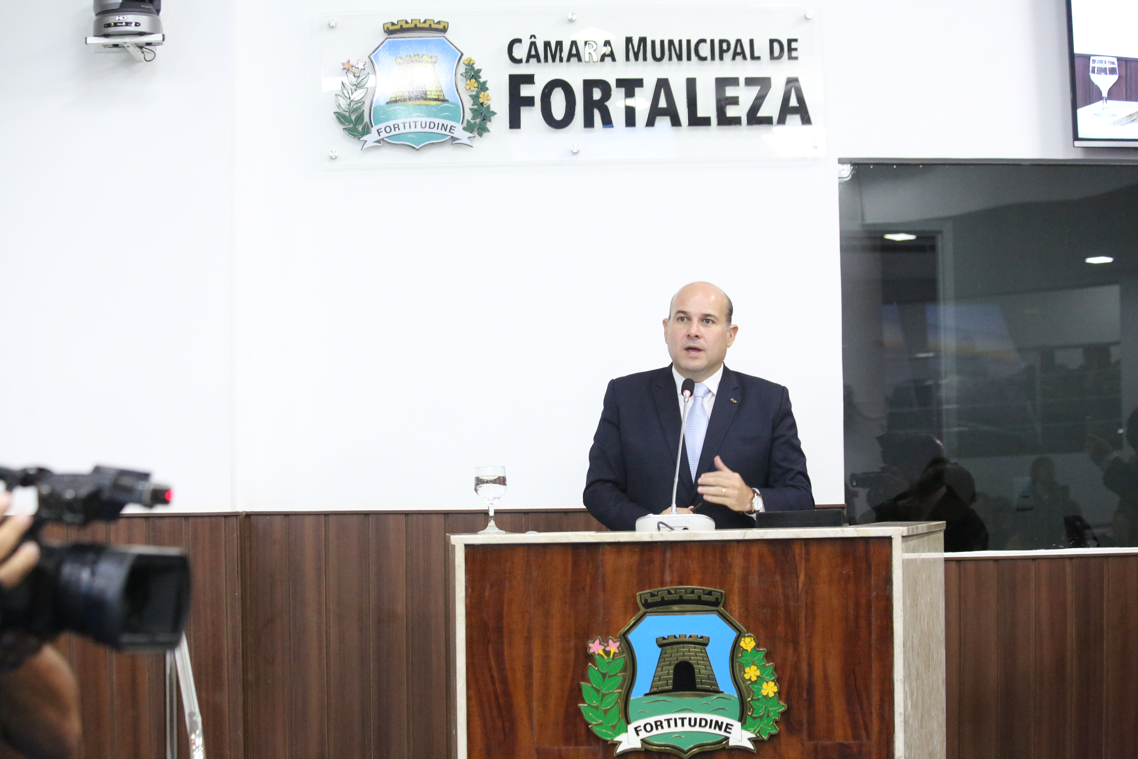 prefeito falando ao microfone em plenária da câmara municipal